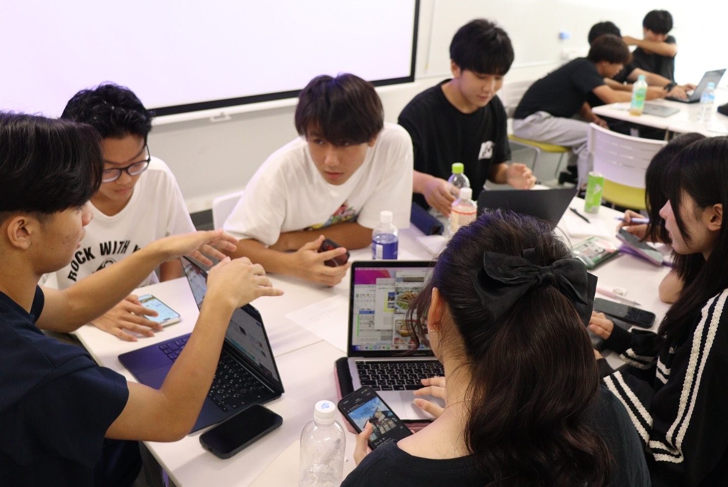 教室でノートPCを囲み、企画について話し合う高校生たち