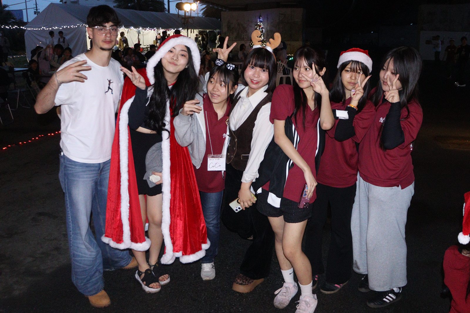 夕暮れの沖縄クリスマスマーケット会場に立つサンタ帽姿の高校生スタッフ